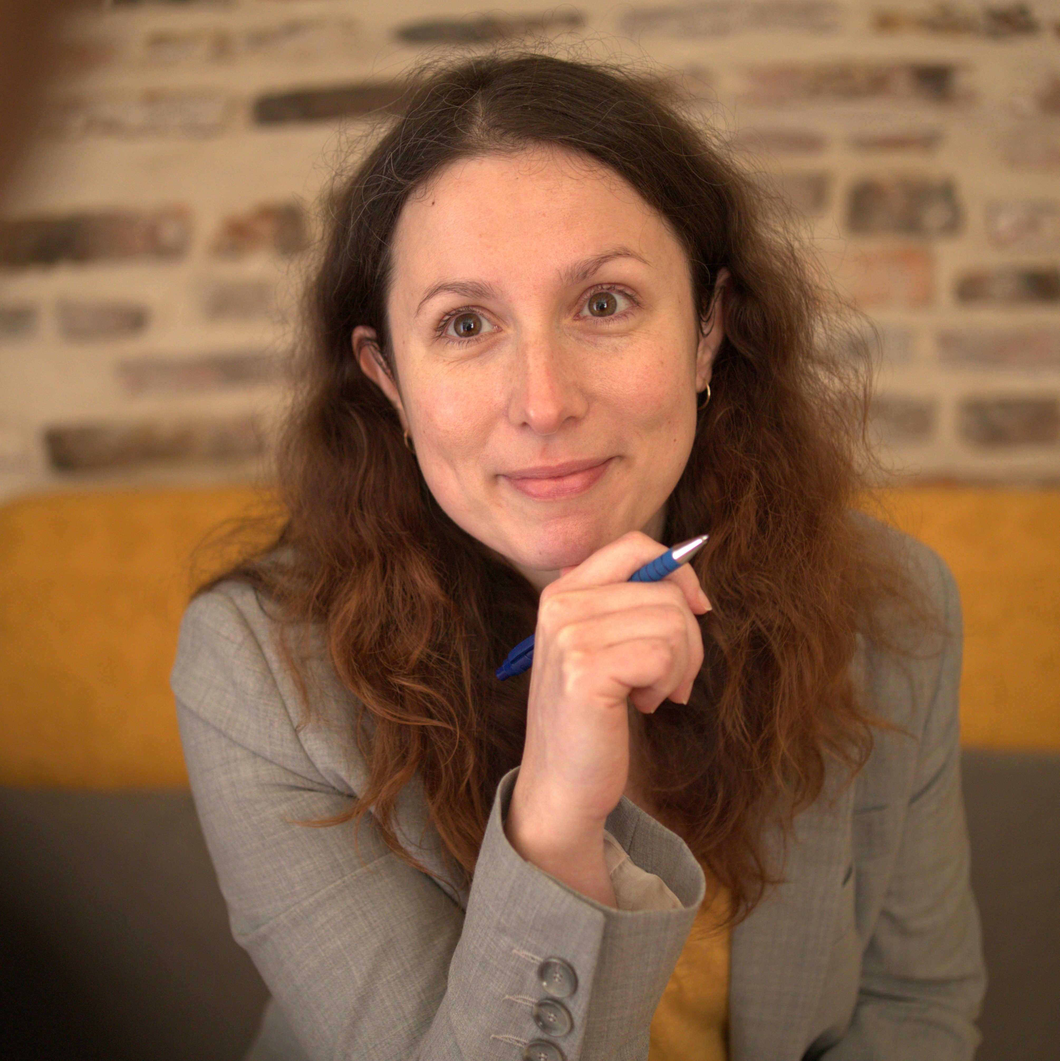 Shaïna regarde l'objectif, elle est en pleine consultation, un stylo à la main, la main sur le menton.